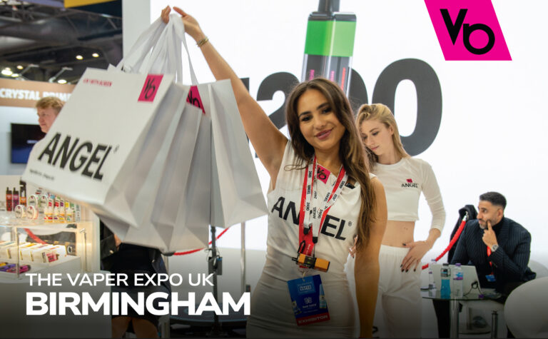 Anchors at Vaper Expo UK 2024 holding Angel® bags with Angel® products displayed in the background.